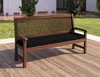 A wooden bench with a black cushion is placed on a wooden deck outdoors, with greenery and a building in the background. Produktbild-Vorschau