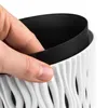 A hand is shown holding the edge of a black insert inside a white, wavy-patterned planter. Anteprima dell’immagine prodotto
