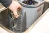 A hand is holding a glass pitcher under running water in a sink, next to a glass washing device. Podgląd zdjęcia produktu