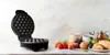 An open waffle maker is shown on a marble countertop, with a selection of fruits, bread, and jars of preserves arranged to the right. Náhľad obrázku produktu