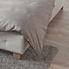 A close-up view of a duvet cover draped over the edge of a bed, showing the texture of the fabric and the wooden legs of the bed frame. Produktbild-Vorschau