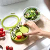 A hand is shown placing a lid on a green food container, which is part of a salad box set. The container holds cherry tomatoes and mozzarella balls. A larger salad bowl is visible in the background. Produktbild-Vorschau
