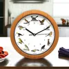 A clock with bird illustrations on a table, with a bowl of tomatoes and a purple napkin in the foreground. Produktbild-Vorschau