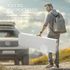 A man is carrying a folded white table with a backpack on his back, standing on a dirt road with a car in the background. Produktbild-Vorschau