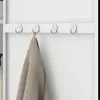 A close-up view of a white cabinet with four metal hooks on a white shelf. A beige towel is hanging on the second hook from the left. Náhled obrázku produktu