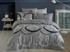 A bed with grey bedding featuring a circular pattern, set against a dark blue wall. Náhľad obrázku produktu