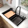 A modern kitchen sink with accessories, set against a window with greenery outside. Náhľad obrázku produktu