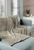 A plush blanket with a leaf pattern draped over a gray sofa and ottoman in a living room setting. Produktbild-Vorschau