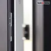 A close-up view of a door lock mechanism, specifically a strike plate, attached to a dark-colored door frame. Podgląd zdjęcia produktu