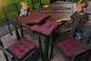 Two children are sitting at a wooden table outdoors, with burgundy seat cushions on chairs around the table. Produktbild-Vorschau