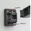 Close-up of a black mounting bracket with screws being inserted, indicating assembly or installation. Produktbild-Vorschau