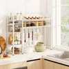 A white kitchen shelf unit filled with jars, utensils, and bowls, placed on a countertop next to a sink and window. Produktbild-Vorschau