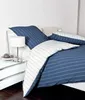 A neatly made bed with blue and white striped bedding, a bedside table with a lamp and decorative balls. Produktbild-Vorschau