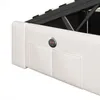 Close-up of a white upholstered bed frame with a lifted mattress mechanism, showing built-in USB charging ports and storage compartments. Produktbild-Vorschau