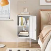 A white metal nightstand with an open door, displaying books and decorative items, next to a bed. Voir les images du produit