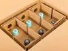 A cardboard box with dividers, holding six bottles. Some bottles have light blue caps with 'DMZ' written on them, and others have black caps with a symbol. Náhled obrázku produktu