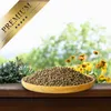 A bowl of birdseed sits on a wooden surface with a blurred background of greenery and flowers. Produktbild-Vorschau