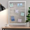 A white framed photo holder with wires and clips, displaying several small photos, is placed on a desk next to a steaming cup of coffee and a desk lamp. A potted plant is visible to the right. Náhled obrázku produktu