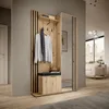 A modern hallway with a wooden wardrobe featuring a mirror, coat hooks, a shelf, and a shoe cabinet with a cushion. The background shows a glimpse of a living room with a sofa and a cityscape view through a large window. Produktbild-Vorschau