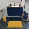 A bathroom scene featuring a blue vanity, a yellow trash can, and a yellow bath mat. Podgląd zdjęcia produktu