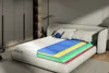 A cutaway view of a mattress showing its different layers, placed on a bed in a bedroom setting. Podgląd zdjęcia produktu