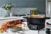 A kitchen counter setting with a soup maker, a bowl of tomato soup, bread, and ingredients like tomatoes, garlic, and chili peppers. Podgląd zdjęcia produktu