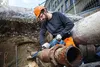 A construction worker is using a reciprocating saw to cut a large, rusty pipe in an excavation site. Anteprima dell’immagine prodotto