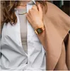 A person wearing a white shirt, a tan scarf, and a gold watch. Produktbild-Vorschau
