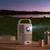 A portable projector is set up on a wooden table outdoors at dusk, with a lake and forest in the background. Produktbild-Vorschau