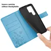 A hand is holding a black phone case over an open blue wallet-style phone case with card slots and a floral design. Produktbild-Vorschau