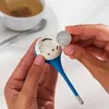 A person is inserting a coin battery into a blue and white digital thermometer. A cup of tea is in the background. Anteprima dell’immagine prodotto