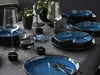 A table setting with blue and black stoneware plates and bowls, wine glasses, and small candle holders. Produktbild-Vorschau