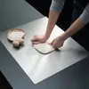 A person is kneading dough on a stainless steel cutting board, with a bowl of flour and eggs nearby. Produktbild-Vorschau