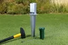 A ground sleeve for a square post, along with a hammer and a wrench, are laid out on a grassy lawn. Produktbild-Vorschau