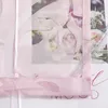 A close-up view of a pink sheer curtain with a floral cut-out pattern, layered over a magazine or printed material featuring floral imagery. Produktbild-Vorschau