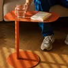 A person's hand is reaching for a glass of water on an orange side table next to a book. The person is wearing blue pants and gray sneakers. Produktbild-Vorschau
