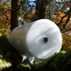A roll of bubble wrap is placed in a forest setting with mossy rocks and autumn foliage. Produktbild-Vorschau