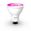 A white smart LED light bulb with a pink glow at the top, set against a white and light gray background. Produktbild-Vorschau