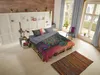 A bedroom with a bed made of pallets, decorated with a colorful mandala duvet cover. There are plants, a lamp, and a rug. Produktbild-Vorschau