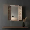A mirror with shutter-style side panels is mounted on a dark gray wall above a wooden console table. A black vase with dried grass is on the table. Náhled obrázku produktu