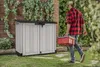 A man is carrying a red toolbox towards a gray storage shed in a garden. Náhled obrázku produktu