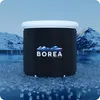 A black foldable ice bath tub with a white lid sits on a surface covered in ice cubes, with snow-capped mountains and a body of water in the background. Produktbild-Vorschau