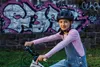 A young girl wearing a helmet and riding a bicycle in front of a graffiti-covered wall. Voir les images du produit