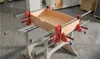 A wooden drawer is being assembled and held together by multiple clamps on a workbench. Náhľad obrázku produktu