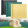 Three rolled-up privacy screens in different colors (anthracite, green, yellow) are shown above a miniature house and a green privacy screen fence in a garden setting. Produktbild-Vorschau