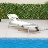 A white lounge chair is placed on a tiled patio next to a swimming pool, with a green leafy fence in the background. Náhled obrázku produktu