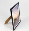 A black picture frame with a beach scene photo, standing on a white surface. Produktbild-Vorschau