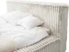 A close-up view of a bed with white bedding and a light gray corduroy headboard. Produktbild-Vorschau