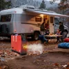 A family is having a meal outdoors next to a camper van, with a red diesel heater in the foreground emitting smoke. Náhled obrázku produktu