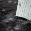 A close-up of a dark gray faux fur rug with a piece of distressed white wood in the foreground. Produktbild-Vorschau
